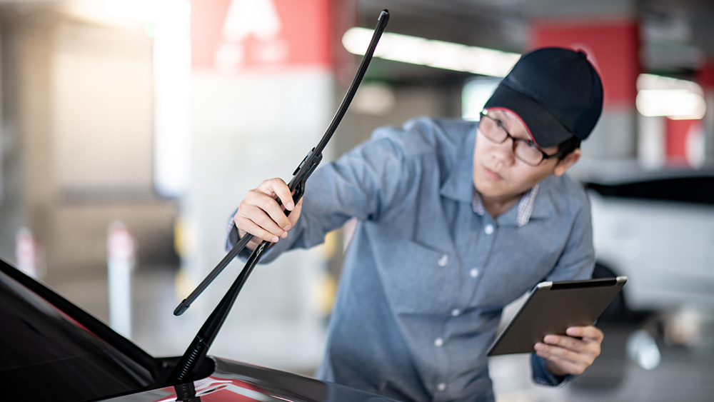 Young Asian auto mechanic holding digital tablet checking windsh